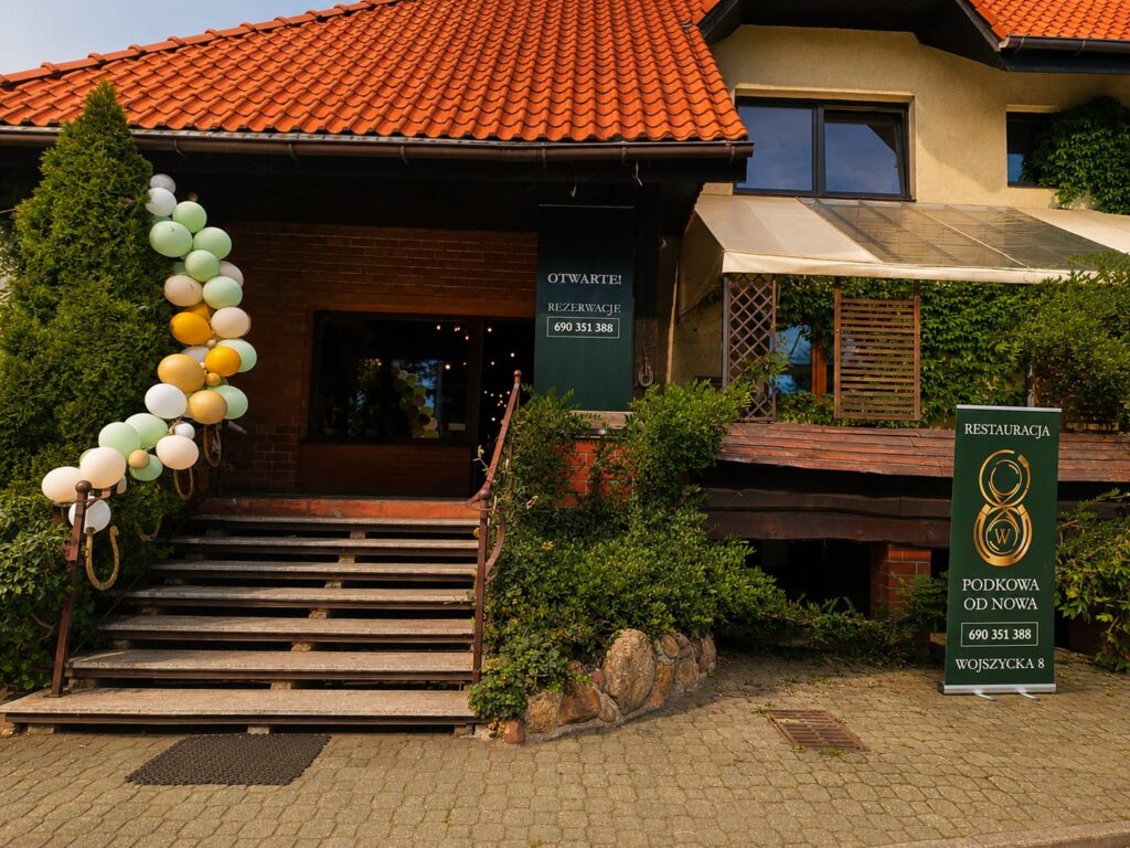 Wejście do restauracji Podkowa od Nowa — dom z czerwonym dachem, kamienne schody i balony